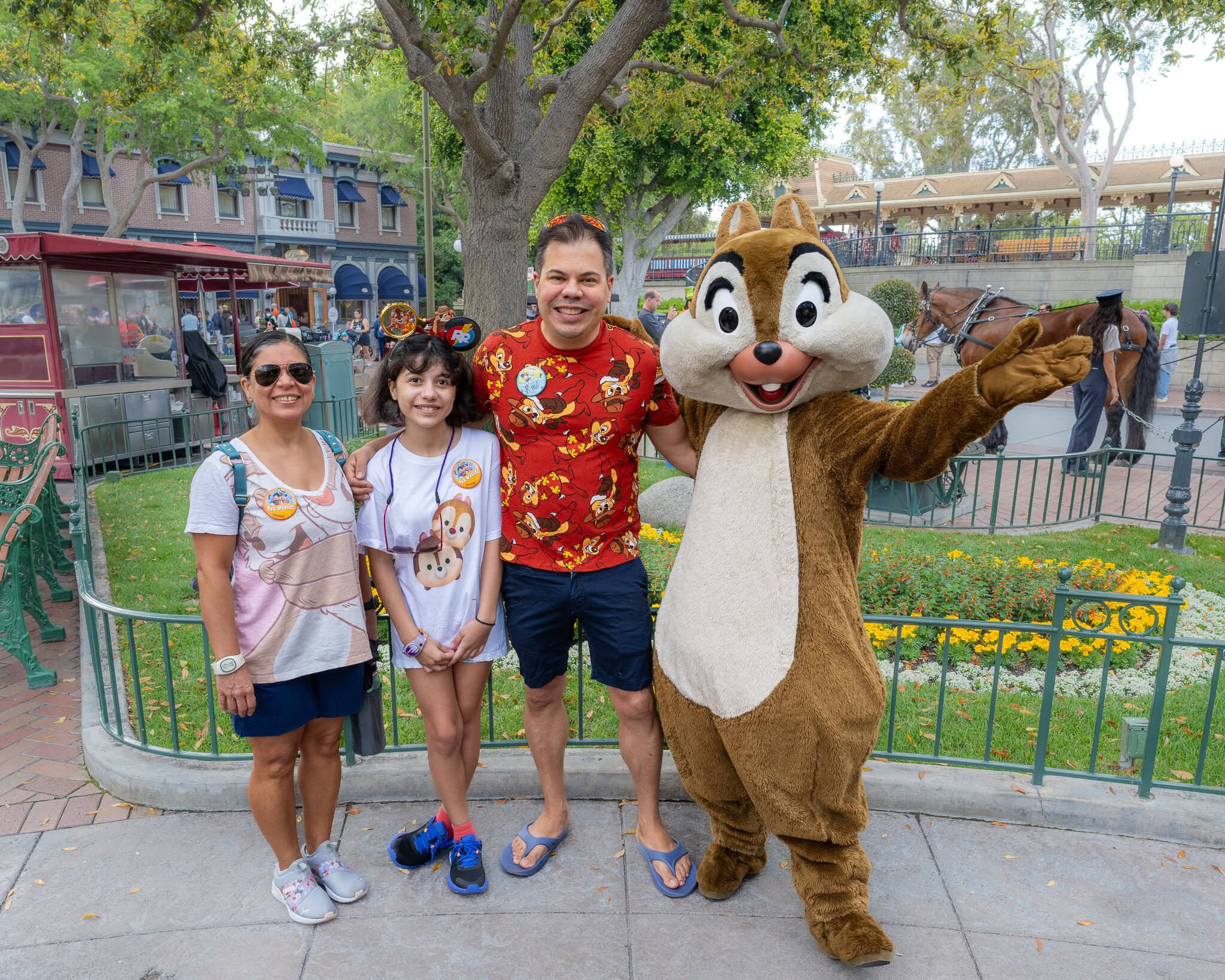 Family posing with Chip from Chip and Dale at Disneyland, featuring vibrant greenery and Main Street in the background.