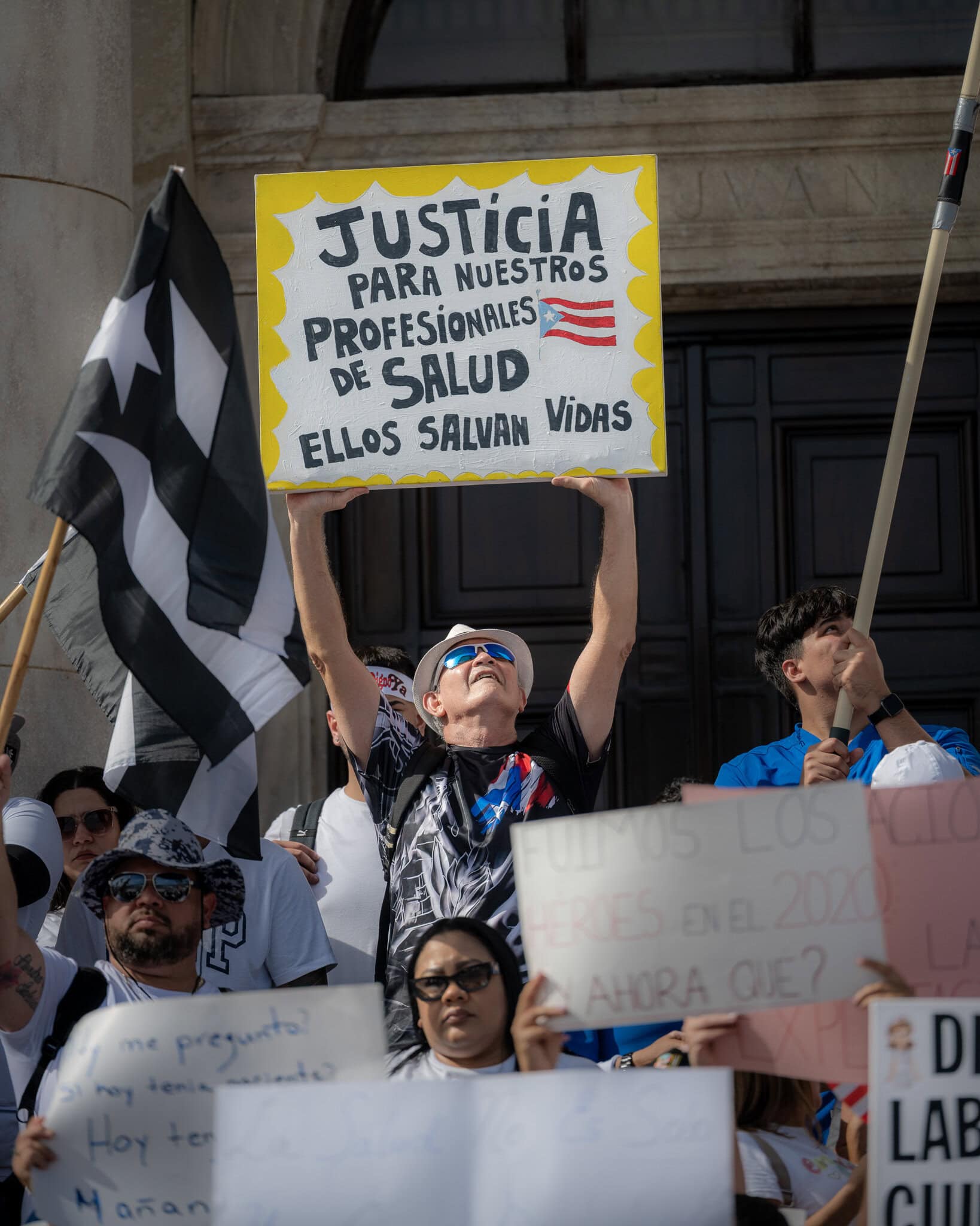 Protester holding a sign that reads “Justicia para nuestros profesionales de salud” at El Capitolio.