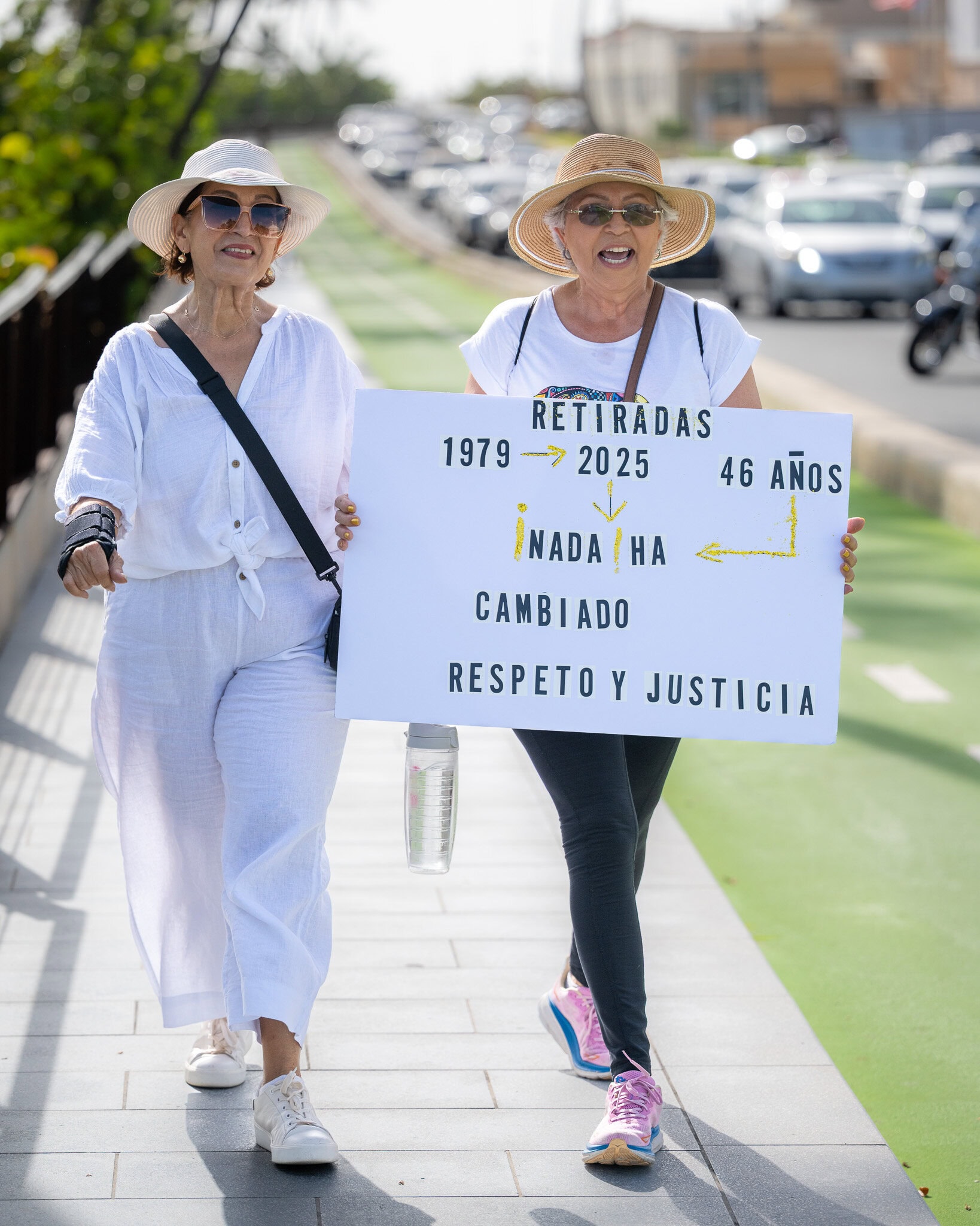 Two retired women walking with a sign that reads “Retiradas 1979–2025, nada ha cambiado” during a protest.